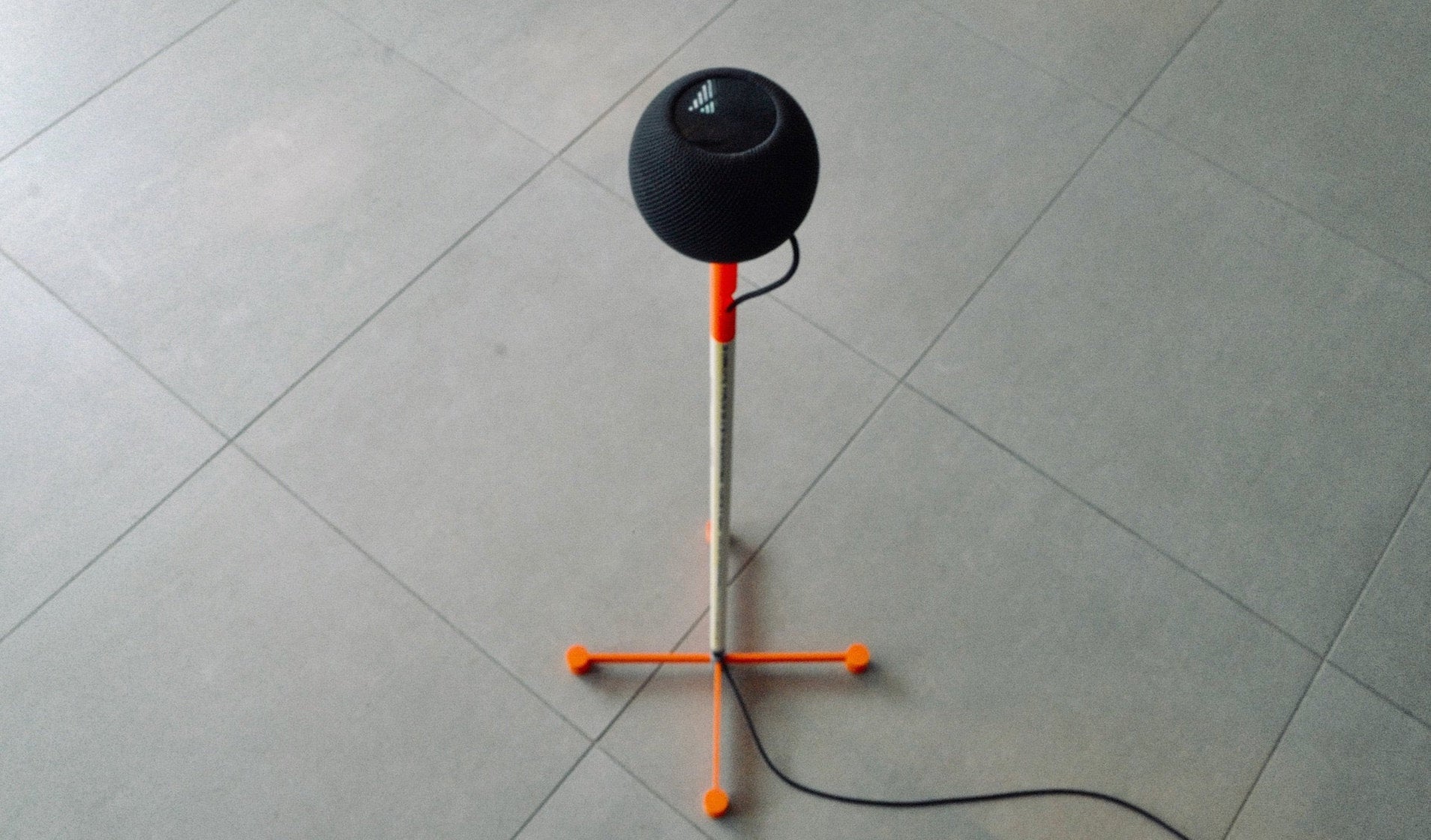 3D-printed DIY HomePod floor stand with an orange printed base and PVC post, holding a black Apple HomePod