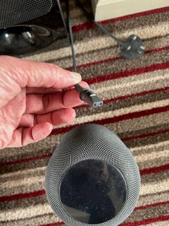 The photo shows the small end of a Black HomePod cable that has been removed. In the background, the larger UK, three-pronged plug top is visible. 