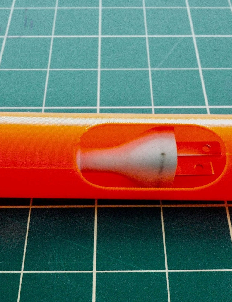 An orange 3D-printed prototype part held on a green cutting mat, the translucent internal form visible through the opening