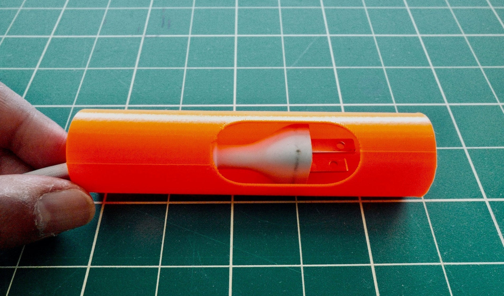 An orange 3D-printed prototype part held on a green cutting mat, the translucent internal form visible through the opening